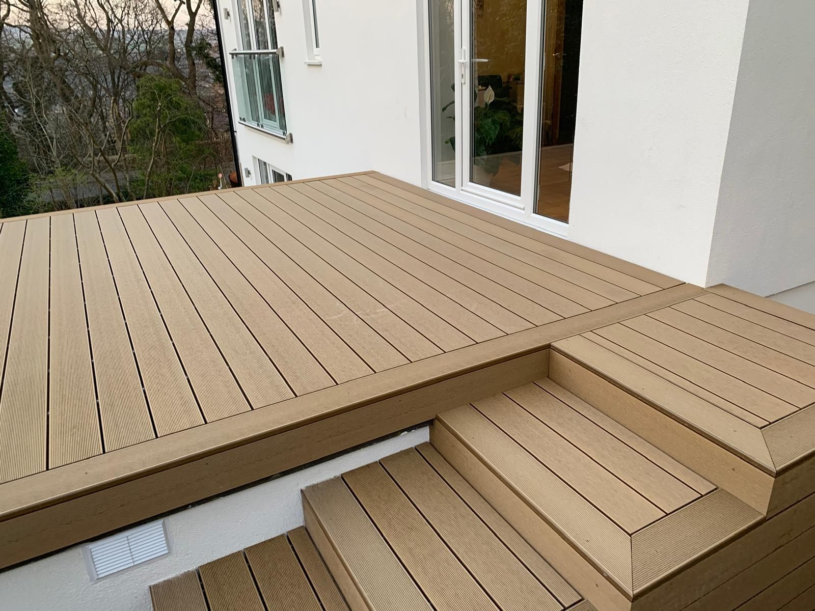 Beige composite decking and matching steps beside a white house